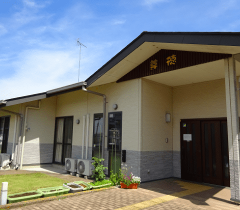 平屋建ての介護施設の建物外観。玄関前にはベンチと花壇がある。
